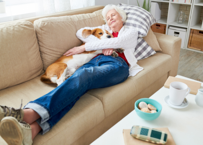 Starsza kobieta leży z psem na kanapie.
